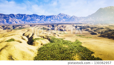 Expansive desert terrain unfolds under a bright blue sky, with verdant patches of vegetation contrasting against rugged mountains in the distance, creating a serene and captivating vista. 130362957