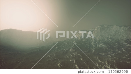 Mist drapes over majestic mountains as dawn breaks, casting a soft glow across the rugged landscape. The air feels alive with the promise of a new day in this breathtaking natural setting. 130362996