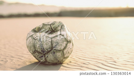 A weathered soccer ball lies abandoned on the sandy beach, illuminated by the warm colors of sunset. The sun casts a soft glow, creating a serene atmosphere around the forgotten toy. A weathered soccer ball lies abandoned on the sandy beach, illuminated by the warm colors of sunset. The sun casts a soft glow, creating a serene atmosphere around the forgotten toy. 130363014