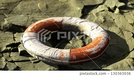 A vibrant lifebuoy lays on a sun drenched, cracked shoreline. The setting captures the essence of tranquility, natures beauty, and the calmness of early morning. A vibrant lifebuoy lays on a sun drenched, cracked shoreline. The setting captures the essence of tranquility, natures beauty, and the calmness of early morning. 130363036