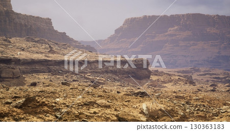 Vast stretches of rocky desert reveal towering cliffs under a hazy sky, with earth tones creating a mesmerizing contrast that invites exploration and adventure in this tranquil wilderness. 130363183