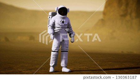 An astronaut stands on the red planets surface, surrounded by rocky terrain and dusty horizons. The Martian atmosphere creates a hazy backdrop for this extraordinary exploration. 130363187