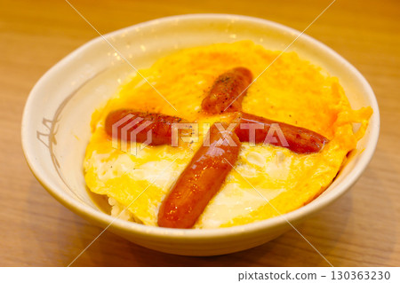 A bowl of rice topped with a fried egg and grilled sausages, seasoned with pepper. A bowl of rice topped with a fried egg and grilled sausages, seasoned with pepper. 130363230