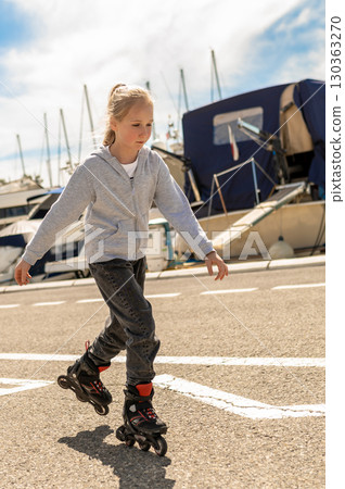 Happy child on rollerblades riding by boats at harbor spending free time Happy child on rollerblades riding by boats at harbor spending free time 130363270