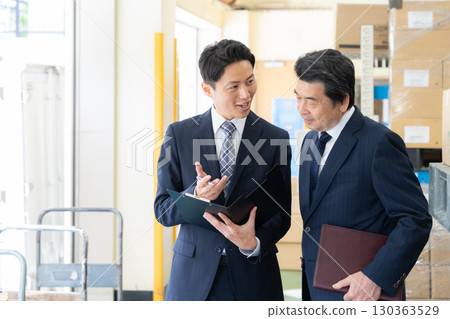 Middle-aged businessmen having a meeting in a warehouse Middle-aged businessmen having a meeting in a warehouse 130363529