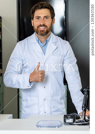 Dark-haired bearded pharmacist in a lab coat looking confident and contented 130363580