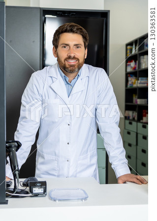Caucasian man in lab coat standing at the counter in the pharmacy Caucasian man in lab coat standing at the counter in the pharmacy 130363581