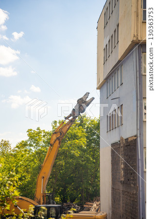 Demolition excavator using hydraulic jaws to dismantle a concrete building at a construction site. Concept of heavy machinery, structural teardown and industrial development. 130363753