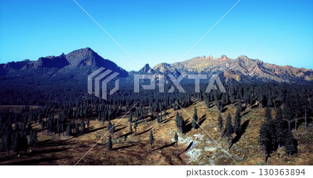 Expansive landscape features rolling hills and towering mountains bathed in sunlight. Lush evergreen trees blanket the ground, creating a tranquil haven in natures embrace. Expansive landscape features rolling hills and towering mountains bathed in sunlight. Lush evergreen trees blanket the ground, creating a tranquil haven in natures embrace. 130363894