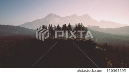 Vibrant trees stand proudly atop a rugged cliff, framed by majestic mountains under a pastel sky. The serene landscape captures the essence of natures beauty at dusk. Vibrant trees stand proudly atop a rugged cliff, framed by majestic mountains under a pastel sky. The serene landscape captures the essence of natures beauty at dusk. 130363895