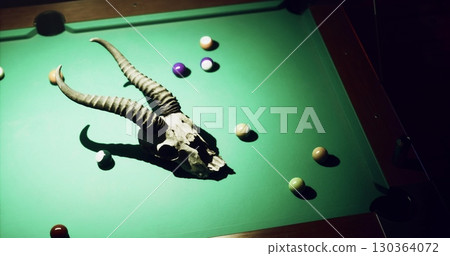 A striking setup featuring a horned skull placed on a green billiard table surrounded by colorful balls, creating a captivating and unusual atmosphere in the dimly lit space. A striking setup featuring a horned skull placed on a green billiard table surrounded by colorful balls, creating a captivating and unusual atmosphere in the dimly lit space. 130364072