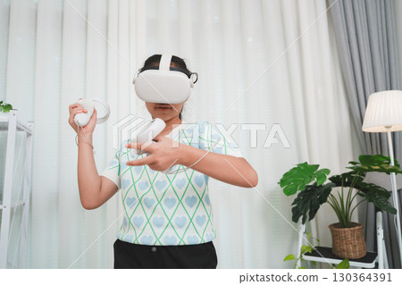 Asian girl wearing VR headset, playing an immersive video game with controllers in a modern room. Asian girl wearing VR headset, playing an immersive video game with controllers in a modern room. 130364391