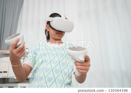 Wearing VR goggles, girl uses controllers to navigate digital world. Shows new generation interaction immersive technology and gaming. Wearing VR goggles, girl uses controllers to navigate digital world. Shows new generation interaction immersive technology and gaming. 130364396