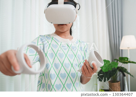 Young girl using a VR headset and controllers for immersive learning at home. Young girl using a VR headset and controllers for immersive learning at home. 130364407