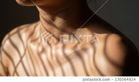 Close-up of a woman's shoulder and neck, illuminated by soft light casting intricate shadows, highlighting skin texture and creating a serene, artistic atmosphere 130364924