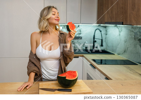 A sensual woman enjoys a slice of juicy watermelon in a modern kitchen. Confident, playful, and radiant, she savors the moment with a hint of summer flirtation. A sensual woman enjoys a slice of juicy watermelon in a modern kitchen. Confident, playful, and radiant, she savors the moment with a hint of summer flirtation. 130365087