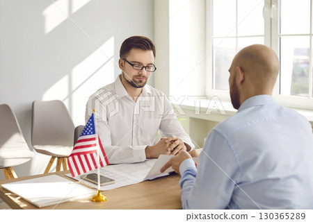 Man at United States of America Consulate looking at visa application form of young man 130365289