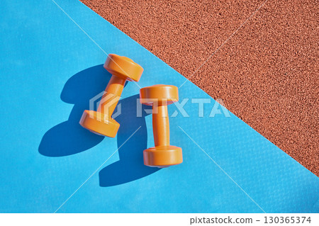 Orange dumbbells and yoga mat at stadium close-up 130365374