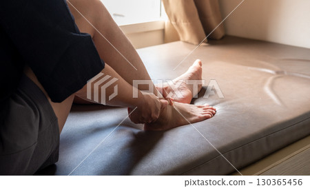 Female hand gripping ankle highlighting foot pain, sports injury, or medical treatment concept 130365456