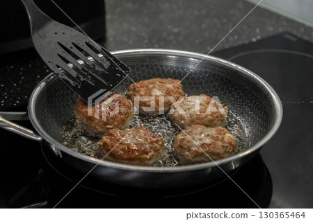 Sizzling golden-brown cutlets cooking in hot oil with a spatula, actively creating a delicious homemade meal in a modern kitchen setting 130365464