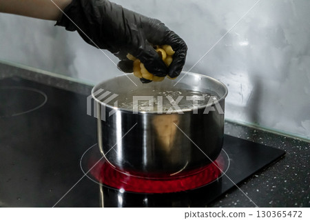 Hand in black glove dropping pasta into boiling water on an electric stove, representing modern kitchen cooking and food hygiene Hand in black glove dropping pasta into boiling water on an electric stove, representing modern kitchen cooking and food hygiene 130365472