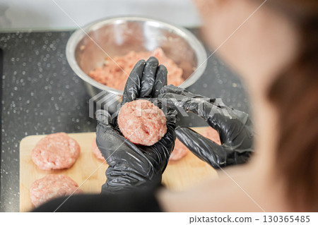 Expert hands in black protective gloves meticulously shaping fresh raw ground meat cutlets, emphasizing hygienic homemade meal preparation for healthy cooking 130365485