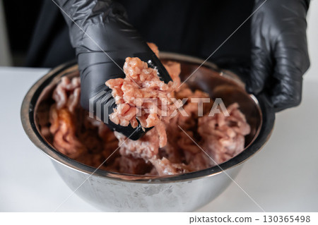 Professional hand wearing a black glove mixing fresh raw ground meat in a stainless steel bowl, essential for preparing delicious cutlets safely 130365498