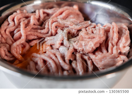 Raw ground pork seasoned with salt and pepper in a metal bowl, with an egg yolk, prepared for making delicious homemade cutlets 130365500