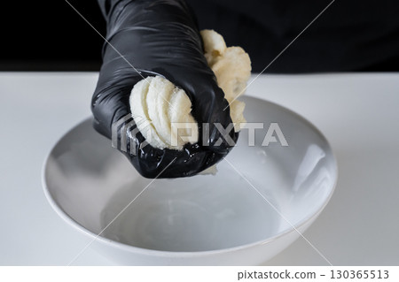 Chef's gloved hand gently squeezing thoroughly soaked white bread over a clean bowl, carefully draining liquid for precise culinary ingredient preparation Chef's gloved hand gently squeezing thoroughly soaked white bread over a clean bowl, carefully draining liquid for precise culinary ingredient preparation 130365513