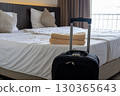Traveler luggage placed beside bed in cozy hotel room symbolizing vacation and relaxation stay 130365643