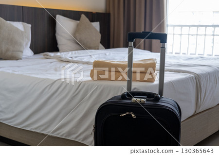Traveler luggage placed beside bed in cozy hotel room symbolizing vacation and relaxation stay Traveler luggage placed beside bed in cozy hotel room symbolizing vacation and relaxation stay 130365643