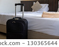 Traveler luggage placed beside bed in cozy hotel room symbolizing vacation and relaxation stay 130365644
