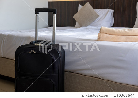 Traveler luggage placed beside bed in cozy hotel room symbolizing vacation and relaxation stay 130365644