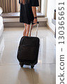 Asian woman dragging suitcase across hotel room floor symbolizing travel, tourism, and vacation 130365651