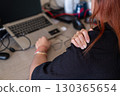 Woman massaging sore shoulders at desk with laptop and office tools highlighting work fatigue 130365654