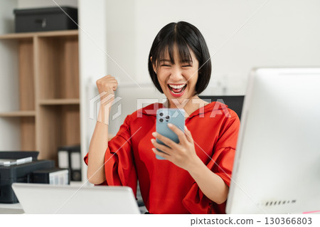 Successful business woman, excited young woman Keeping up arms and showing positive emotions, happy working in modern office on smartphone.. 130366803
