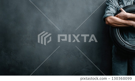 Mechanic Holding Tire Against Dark Wall Background 130368099