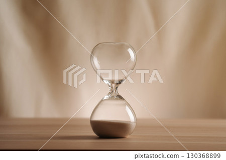 A simple hourglass on a wooden table with a beige backdrop, symbolizing time flow and minimalistic living. Represents timeless themes in a creative, uncluttered presentation for stylish concepts. A simple hourglass on a wooden table with a beige backdrop, symbolizing time flow and minimalistic living. Represents timeless themes in a creative, uncluttered presentation for stylish concepts. 130368899