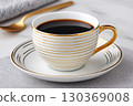 White and gold coffee cup filled with dark coffee sitting on matching saucer 130369008