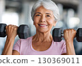 Senior woman lifting weights and smiling at the gym, promoting health and fitness in old age 130369011