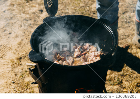 Meat cooking in a large cauldron outdoors over an open fire, a classic outdoor cooking concept for camping and traditional cuisine. Meat cooking in a large cauldron outdoors over an open fire, a classic outdoor cooking concept for camping and traditional cuisine. 130369205