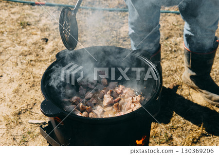 Meat cooking in a large cauldron outdoors over an open fire, a classic outdoor cooking concept for camping and traditional cuisine. Meat cooking in a large cauldron outdoors over an open fire, a classic outdoor cooking concept for camping and traditional cuisine. 130369206