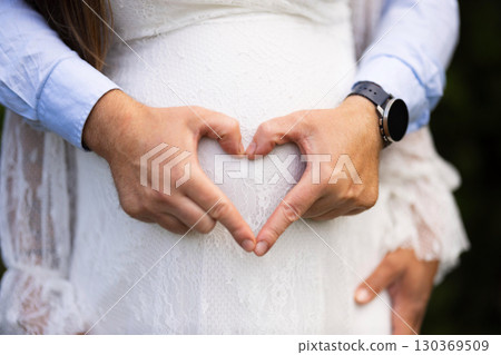 Hands Forming a Heart Over a Pregnant Belly in Soft Lighting 130369509