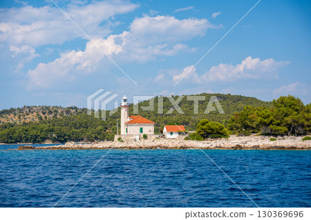 Stone lighthouse with red roof on the rocky coast of Hvar Island, Croatia, surrounded by pine trees and clear blue sea. Navigation, solitude and maritime heritage in the Adriatic. 130369696