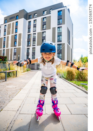 Little girl learning to roller skate for the first time at the age of five. Concept of physical development, balance training and childhood independence through active play. 130369774