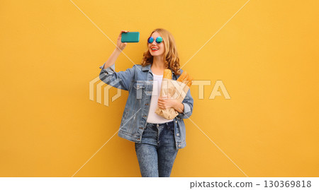 Happy smiling young woman taking selfie with smartphone holds grocery shopping paper bag with bread Happy smiling young woman taking selfie with smartphone holds grocery shopping paper bag with bread 130369818