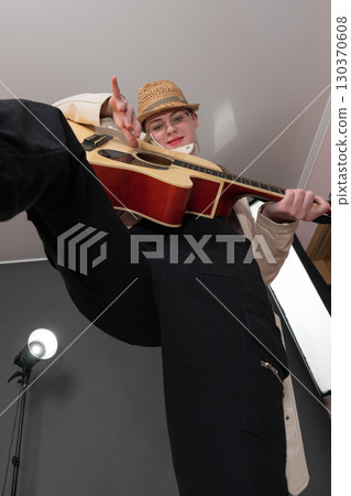 Woman guitarist strumming Spanish six string acoustic guitar, looking at camera. Extraordinary low angle view, wide shot perspective of playful musician. Selective focus on expression female guitarist 130370608
