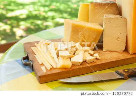 Assortment of sliced and chunked cheeses with knife on wooden cutting board Assortment of sliced and chunked cheeses with knife on wooden cutting board 130370773