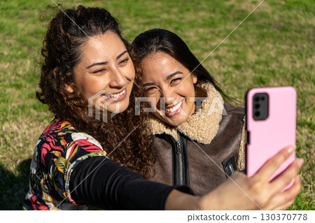 Two smiling young women taking a selfie in the park on a sunny day Two smiling young women taking a selfie in the park on a sunny day 130370778
