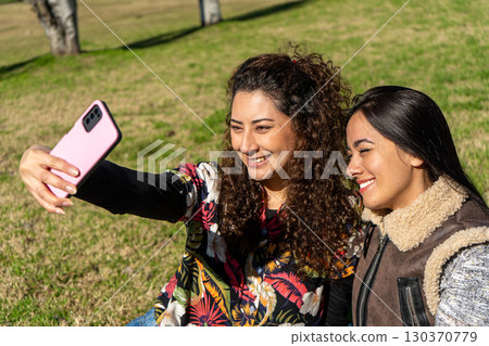 Two smiling young women taking a selfie in the park on a sunny day 130370779